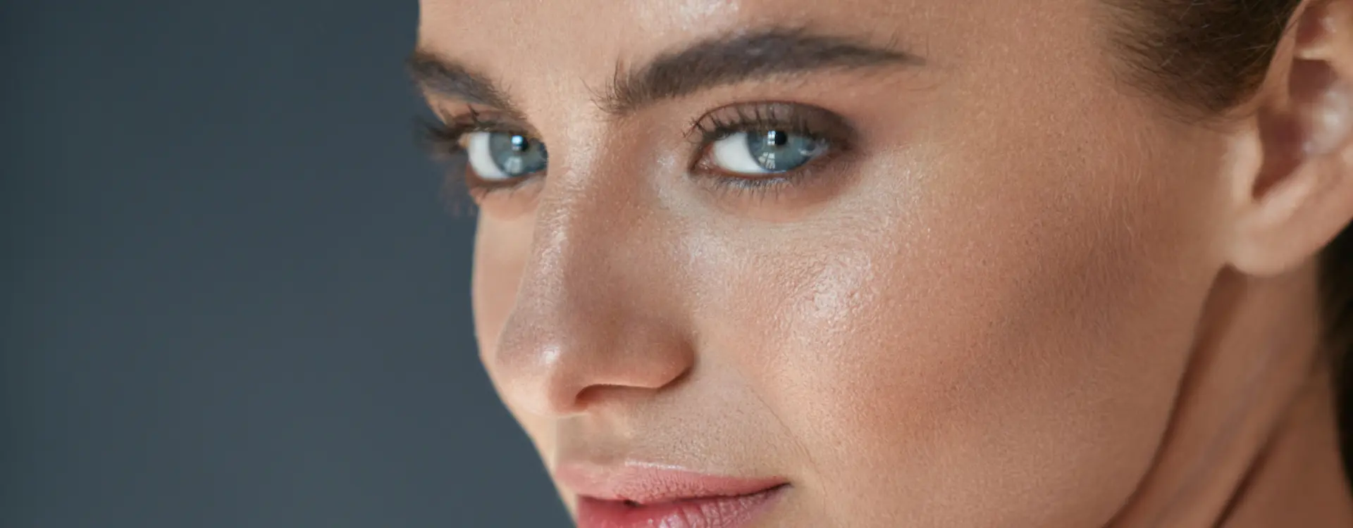 A close-up of a woman’s blue eyes, nose and cheek against a dark grey background, the photo on Bellava’s eyelid surgery page