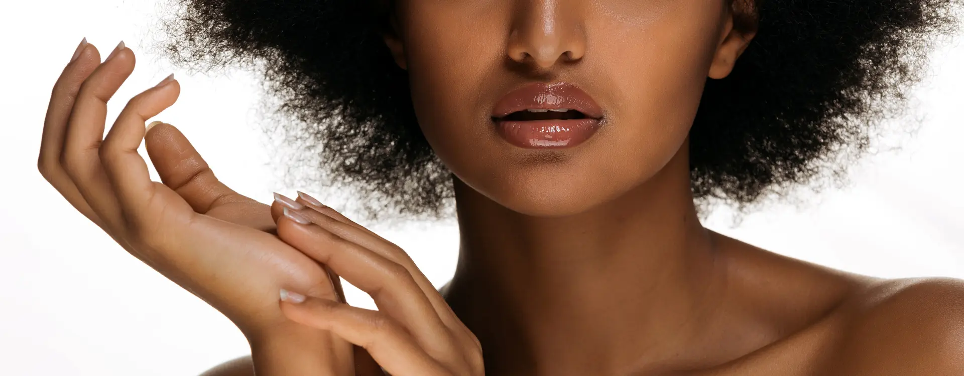 Close-up of a woman’s full, glossy lips with her hands raised beside her face against a white background