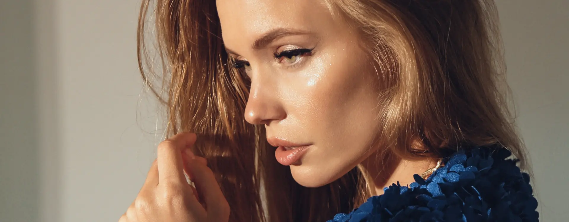 A woman with long honey-brown hair in profile, fingers in a strand of hair, wearing a blue sequinned top, the photo on Bellava’s Radiesse page