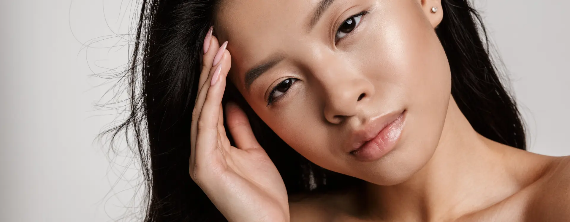 A dark-haired woman resting her fingertips against her brow in front of a pale grey backdrop, the photo on Bellava’s Restylane page