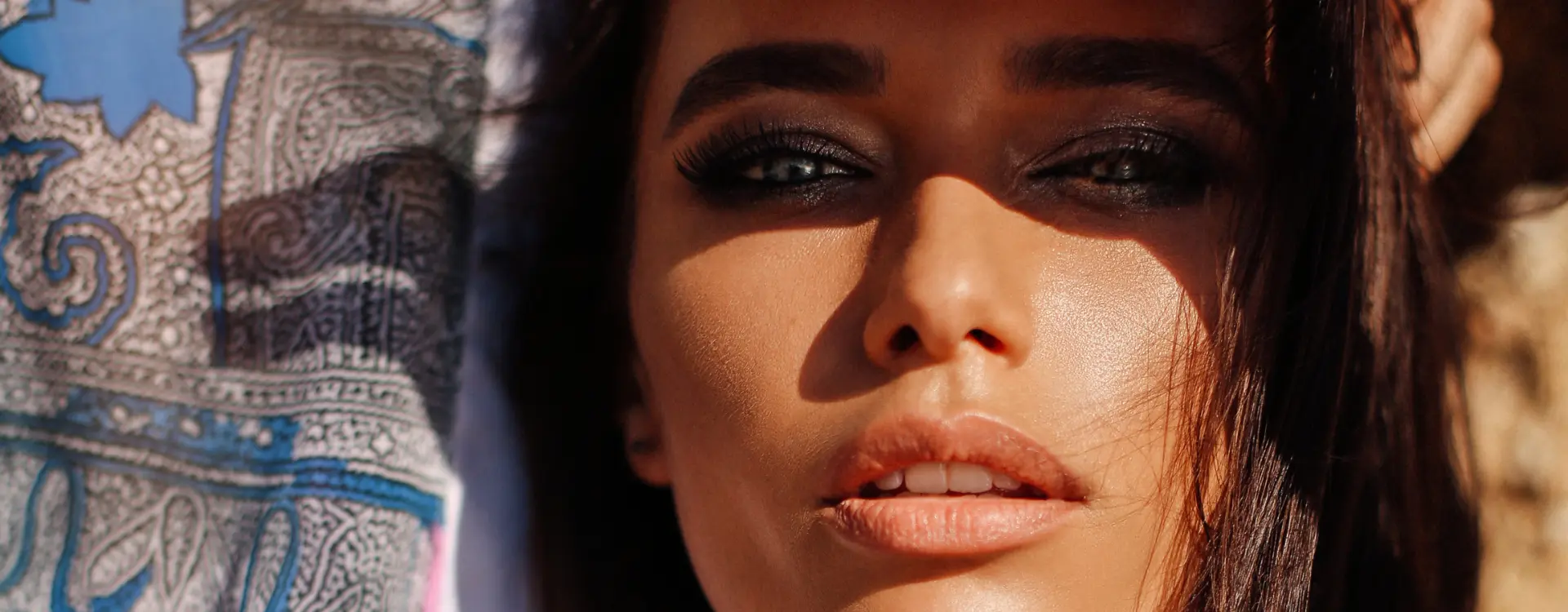 A sunlit close-up of a dark-haired woman’s face beside a blue paisley scarf, the photo on Bellava’s Sculptra page