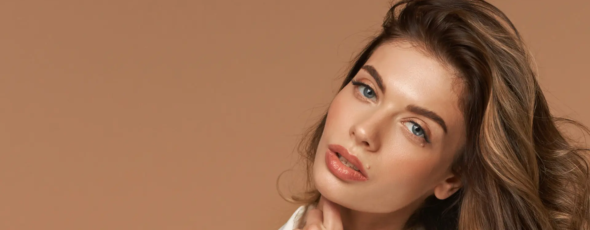 A woman with long wavy brown hair and clear skin against a tan backdrop, the photo on Bellava’s skin rejuvenation page