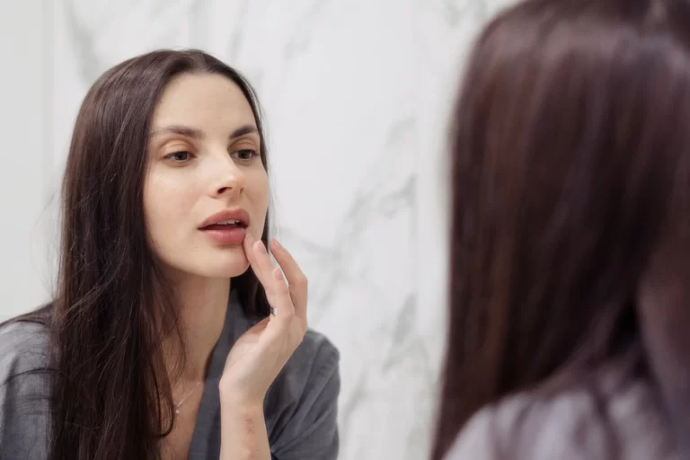 a woman checks her lips in front of the mirror|a woman taking a pill to address reactions duue to lip fillers|a portrait of a beautiful woman