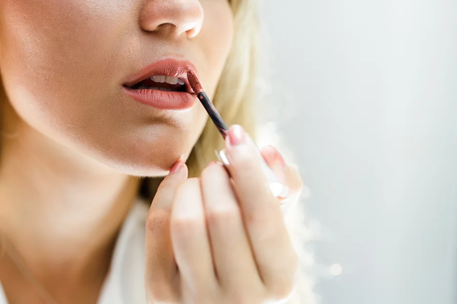 a woman applies lip gloss on her lips