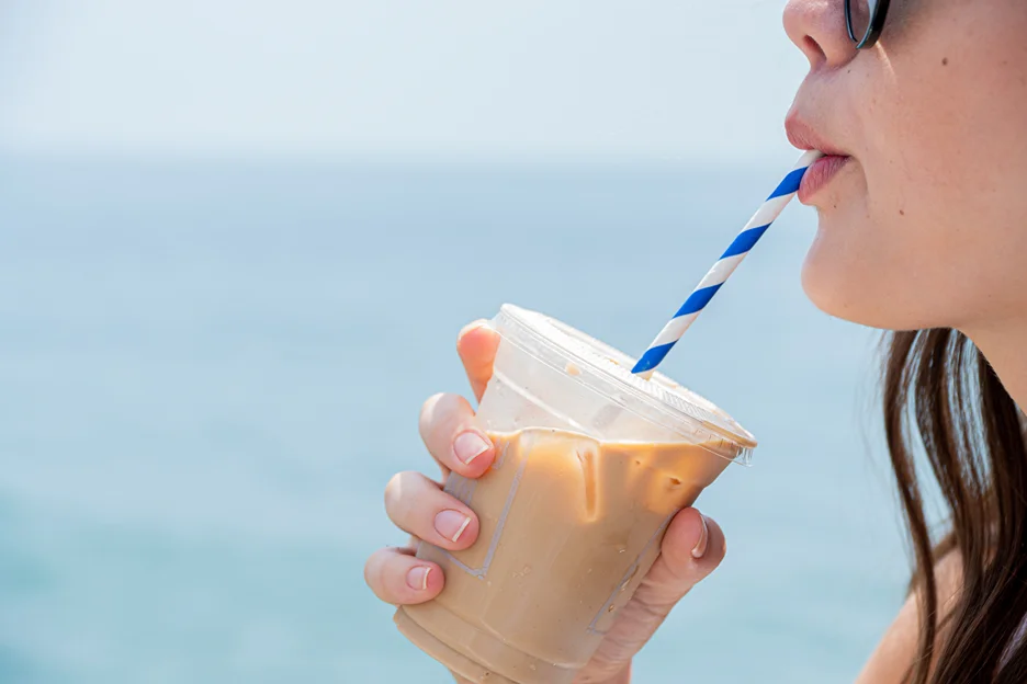 a woman sips from a cup of iced coffee using straw