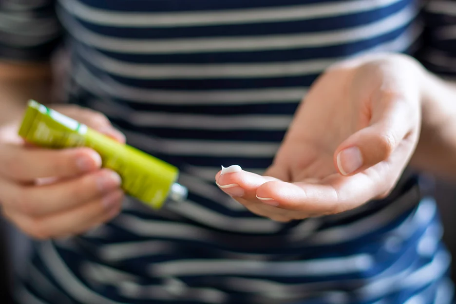 a woman holds topical topical hydrocortisone cream to treat white spot on lip after filler