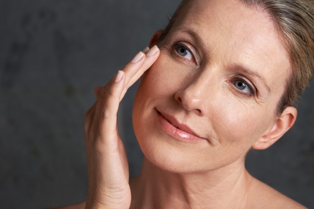Liquid facelift: Middle-aged woman touching her cheek with smooth, rejuvenated skin.