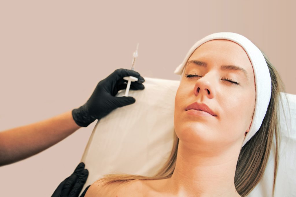 Liquid facelift: Woman lying relaxed as a clinician prepares facial injectable treatment.